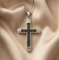 14k white gold black moissanite cross pendant necklace. A silver and gold cross pendant necklace with black gemstone detailing, displayed on a draped beige satin fabric background.