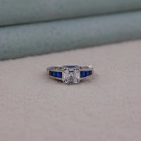 Silver ring with a diamond and blue gemstones on a neutral background