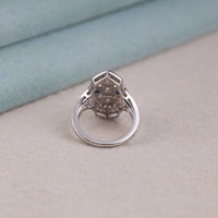 Silver ring with intricate design on a light beige surface