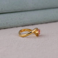 Gold ring with a pink gemstone on a light gray surface