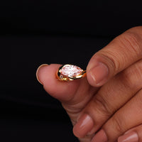 Gold ring with a large diamond held between fingers against a black background