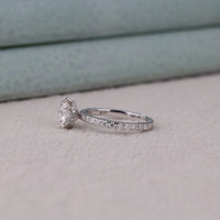 Silver ring with a large diamond and smaller diamonds on the band against a neutral background