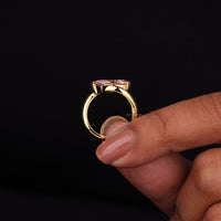 Gold ring with a pink gemstone held by a hand against a black background