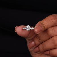Diamond ring held between fingers against a black background