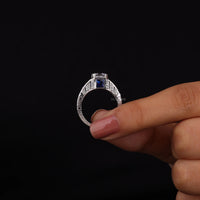 Silver ring with a blue gemstone held between fingers against a black background