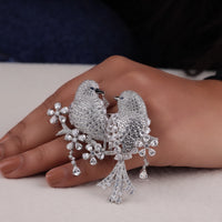 Silver bird-shaped earrings on a hand with a neutral background, Animal-Inspired CZ Brooch – Love Bird Design with Round & Marquise Stones