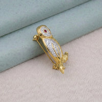 Gold bird-shaped brooch with gemstones on a textured surface