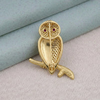 Gold owl brooch with red eyes on a textured surface
