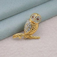 Gold owl brooch with gemstones on a textured surface