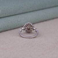 Silver ring with a textured design on a light wooden surface, Oval & Tapered Baguette CZ Starburst Halo Engagement Ring, Vintage Inspired Wedding Jewelry, Elegant Oval Halo Bridal Ring For Women