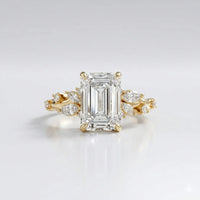 Gold ring with a large diamond and smaller diamonds on the sides against a light gray background
