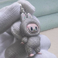 Silver pig-shaped keychain with pink face held by a gloved hand against a light background