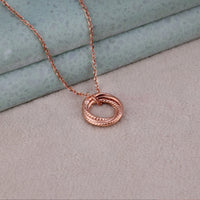 Rose gold necklace with a circular pendant on a textured surface, Elegant Rose Gold Interlocking Ring Necklace, Dainty Gift for Women
