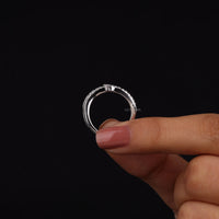 Silver ring held by a hand against a black background