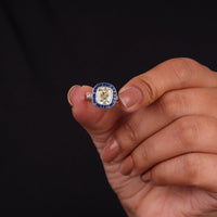 Hand holding a diamond ring with a blue and gold band against a black background, Old Mine Cut CZ Stone Sapphire Halo Ring – Antique Art Deco Vintage Design