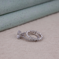 Two silver rings on a textured surface with a light green background, Round Moissanite Engagement Ring with Eternity Wedding Band Set