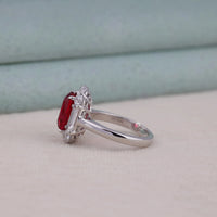 Silver ring with a red gemstone and diamonds on a light background