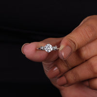 Diamond ring held between fingers against a black background