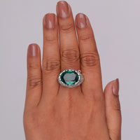 Hand wearing a ring with a green gemstone on a plain background, Green Emerald CZ Oval Ring, Vintage Filigree Antique Style Cocktail & Engagement Ring