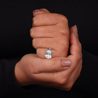 Hand holding a diamond ring with a black background, Toi Et Moi Moissanite Engagement Ring – White Pear & Green Radiant Two Stone Wedding Ring