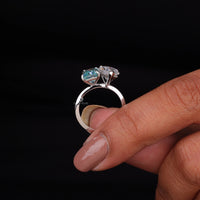 Silver ring with gemstones held by a hand against a black background, White Pear & Green Radiant Cut Moissanite Ring – Toi Et Moi Two Stone Engagement Ring
