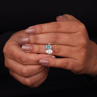 Close-up of a hand holding a diamond ring with a green gemstone on a black background, Green Radiant & White Pear Moissanite Toi Et Moi Ring – Modern Two Stone Engagement Ring