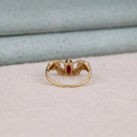  Gold ring with a red gemstone on a light gray background