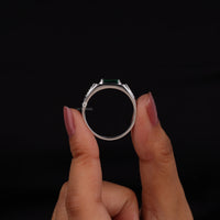 Silver ring with a green gemstone held by a hand against a black background