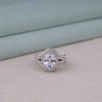 Diamond ring on a light gray surface with a soft blue background, Elegant Oval Moissanite Split Shank Engagement Ring with Halo & Enhancer Wedding Band