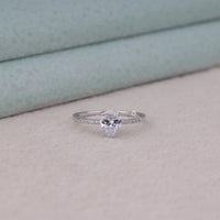 Pear-shaped diamond ring on a light surface with a neutral background, Pear Shape Moissanite Engagement Ring – Pave Diamond Band White Gold Ring