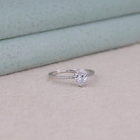 Silver ring with a pear-shaped diamond on a light background, Minimalist Pear Cut Solitaire Ring – Moissanite Pave Band White Gold Engagement Ring