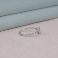 Silver ring with a diamond on a light pink surface, Classic Pear Cut Moissanite Engagement Ring – White Gold Pave Band Bridal Jewelry