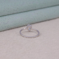 Silver ring with a Pear-shaped gemstone on a textured surface, Pear Shape Solitaire Wedding Ring – Moissanite Pave Band White Gold Setting