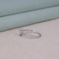 Silver ring with a diamond on a light pink surface, Timeless Pear Cut Moissanite Engagement Ring – Solitaire Pave Band Design