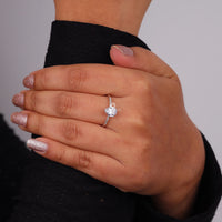 Hand wearing a diamond ring with a plain background, Elegant Pear Cut Moissanite Engagement Ring – Classic Solitaire with Pave Band