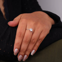 Hand wearing a diamond ring with a blurred background, Pear Cut Solitaire Engagement Ring – Moissanite Pave Band White Gold Wedding Ring