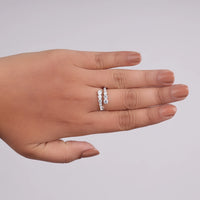 Hand wearing two diamond rings on a light gray background, nontraditional engagement ring, open shank Moissanite, twist bypass ring, moissanite bypass engagement,