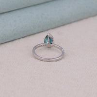 Silver ring with a teardrop-shaped blue gemstone on a light gray surface, Wedding Jewelry, Stylish Moissanite Promise Ring, Durable Pear Shape Bridal Engagement Band.
