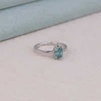 Silver ring with a pear-shaped blue gemstone on a light gray surface, Green & Aqua Pear Cut Moissanite Half Halo Engagement & Wedding Ring, Two Stone Moissanite Toi Et Moi Ring