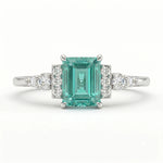 Ring with emerald-cut green gemstone and diamond accents on a white background