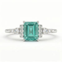 Ring with emerald-cut green gemstone and diamond accents on a white background