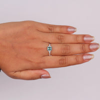 Hand wearing a ring with a green gemstone on a light gray background