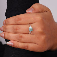 Hand wearing a ring with a green gemstone on a neutral background