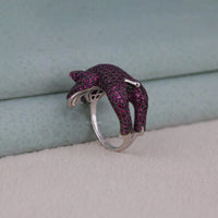 Dolphin-shaped ring with pink gemstones on a light gray surface