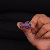 Hand holding a pink and black bear-shaped object against a black background