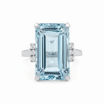 Ring with a large emerald-cut blue gemstone and smaller diamonds on a white background