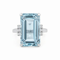 Ring with a large emerald-cut blue gemstone and smaller diamonds on a white background
