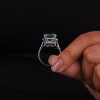 Silver ring with a blue gemstone held by a hand against a black background