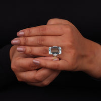 Hand wearing a ring with a large gemstone on a black background