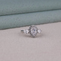 Silver ring with a pear-shaped center stone and smaller stones on a light gray background